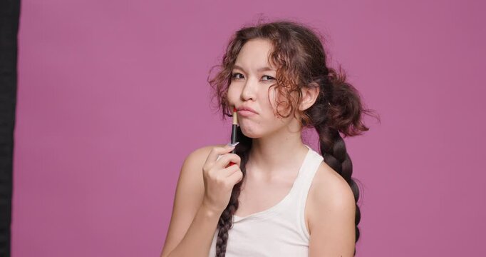 Young Kazakh woman with pen, displays contemplative expression against pink background