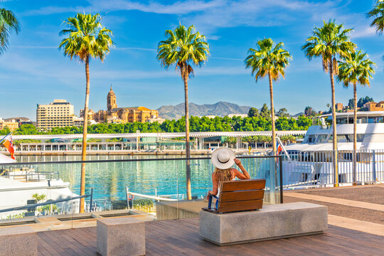 Traveler woman tourist sitting on bench admiring Malaga city view with cathedral, port and palm trees, Travel in Europe, Spain