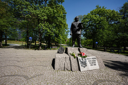 Statue Jerzy Zietek and monument in a city park in Katowice, Poland with sculpture on stone pedestal surrounded by trees and cobblestone walkways