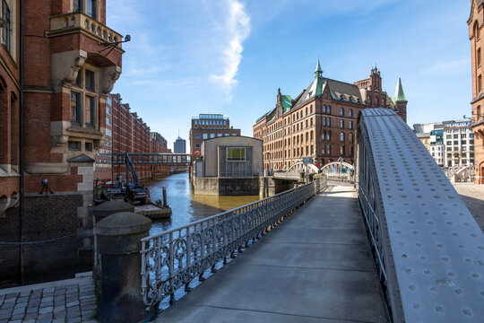 A scenic view of Speicherstadt, Hamburg's iconic warehouse district, showcasing historic brick buildings and iron bridges over the canal.