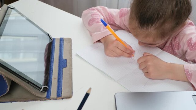 Child doing homework with laptop and notebook at home, hybrid education concept, close up