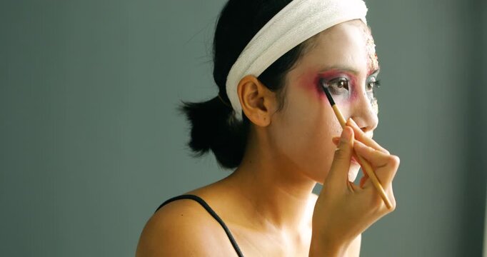 Asian woman applying spooky Halloween zombie makeup with a cosmetic brush