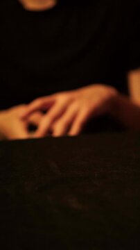 Blurred hand slightly lifting playing cards to check hand during emotional card game and lowering them back onto dark table, gambling and betting tension concept.