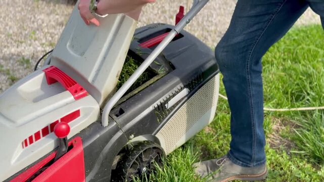 Man emptying full grass catcher of electric lawn mower into a bag in the garden