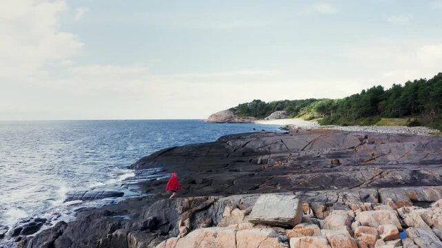 Lonely woman dressed bright sporty clothes jogging early morning. She standing on huge boulders coast on North Sea Telemark, South Norway with raised hands and enjoying sunrise. Active people concept
