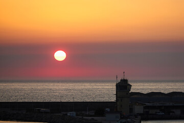 Golden sunset over the sea with industrial port buildings in silhouette. Vivid orange sky at Vila do Conde harbor, Portugal. Scenic evening view of the sun setting over the Atlantic Ocean horizon © Alexander