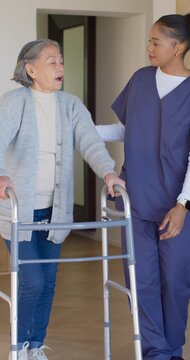 Vertical video: Senior Asian woman placing hands on walker, walking at home to steady, aide helping