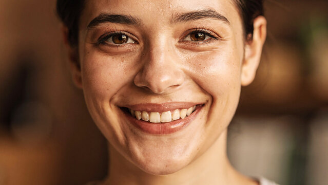 Woman with long hair and a white shirt is smiling. She has a light makeup on her face. Portrait of a tender woman in her 50s wearing a classic white shirt in blank studio backdrop