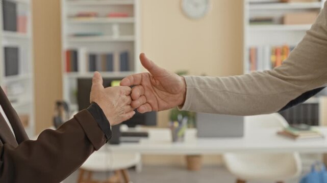 Woman fist bumping with man over office desk in building, hands meeting in greeting; camaraderie teamwork.