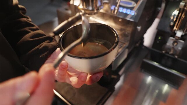 Specialist hands swirling fresh espresso in a glass cup