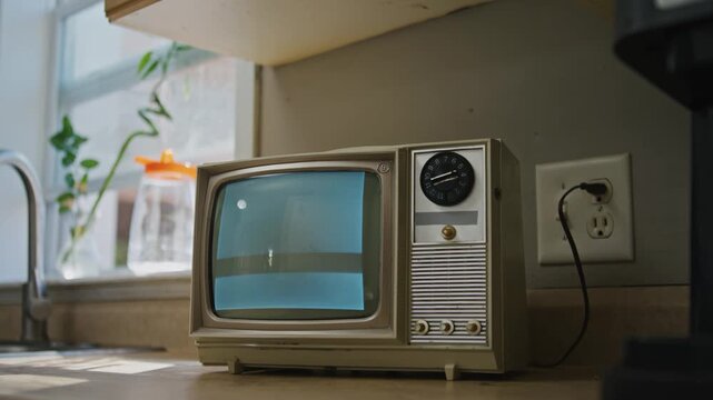 A vintage television sits on an old kitchen counter, casting static amid warm lighting. This charming setup evokes memories of the past with its analog noise and retro decor