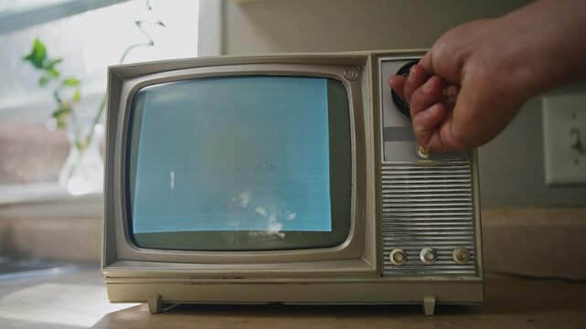 An old black and white television sits on a rustic kitchen counter, showing static noise. Soft light filters through the window, creating a nostalgic atmosphere perfect for Halloween vibes