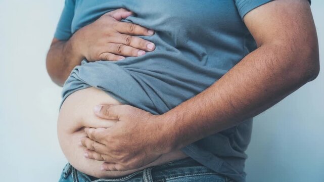 Man in blue t shirt and jeans gently holding bloated stomach showing discomfort and health concern
