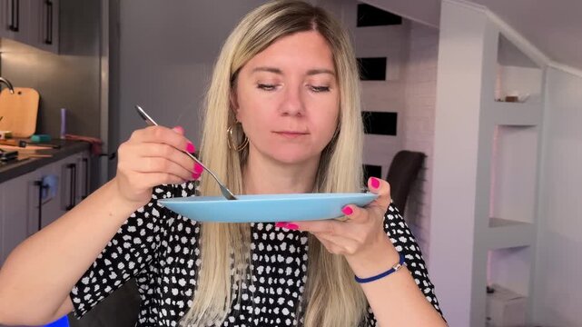 Woman Enjoys Pastry. Blonde Lady Carefully Evaluates Pastry While Relaxing In Modern Kitchen Setting