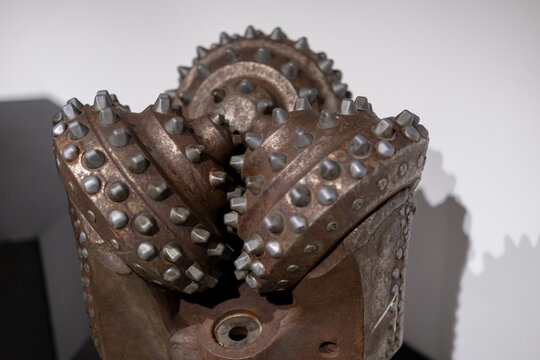 Macro view of a worn and rusted tricone drill bit featuring heavy steel teeth used in the petroleum and mining industry.