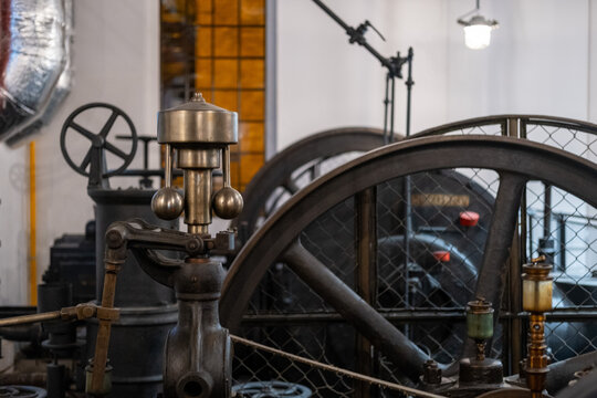 Vintage centrifugal flyball governor and large metal flywheels of a historic industrial steam machine.