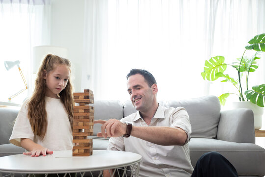 Father and daughter playing wooden block tower game at home. Family bonding activity, child development, learning through play, concentration, and positive parenting in a cozy living room.