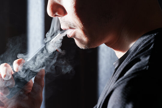 鼻と口からダイナミックに煙を吐き出す喫煙男性。大人の嗜好品と加熱式タバコの煙テクスチャ