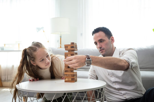 Father and daughter playing wooden block tower game at home. Family bonding activity, child development, learning through play, concentration, and positive parenting in a cozy living room.
