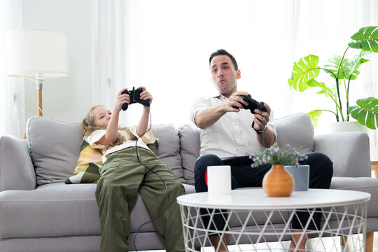 Father and daughter playing video games together at home. Happy family spending quality time, bonding, entertainment, and modern lifestyle in a cozy living room.
