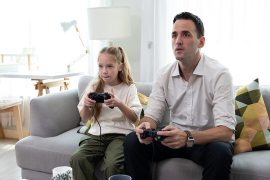 Father and daughter playing video games together at home. Happy family spending quality time, bonding, entertainment, and modern lifestyle in a cozy living room.