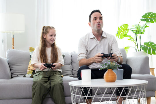 Father and daughter playing video games together at home. Happy family spending quality time, bonding, entertainment, and modern lifestyle in a cozy living room.