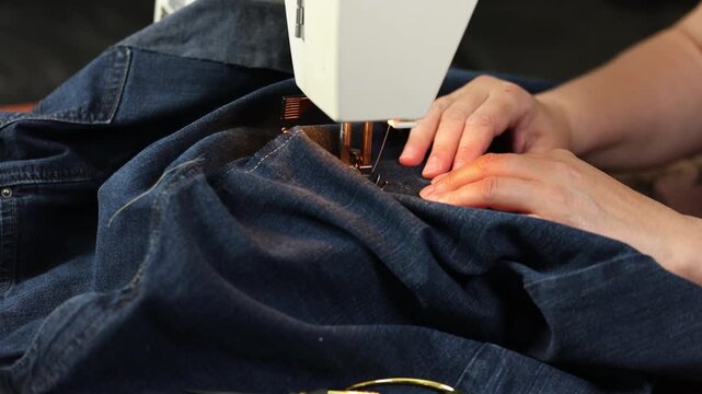 Woman sewing denim fabric close up on sewing machine. Focus on hands and process. Concept of DIY , handmade work
