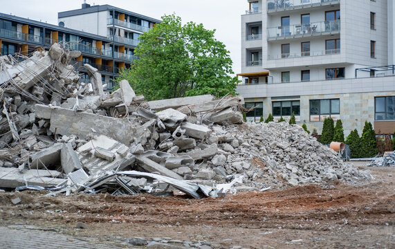 A large pile of broken concrete rubble and twisted metal rebar from a demolished structure sitting in front of a modern residential apartment building.