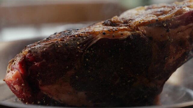 Juicy, grilled ribeye steak steams on a plate. Rich brown crust and visible seasoning highlight its succulent texture. Smoke gently rises, suggesting fresh cooking. Ideal for food blogs