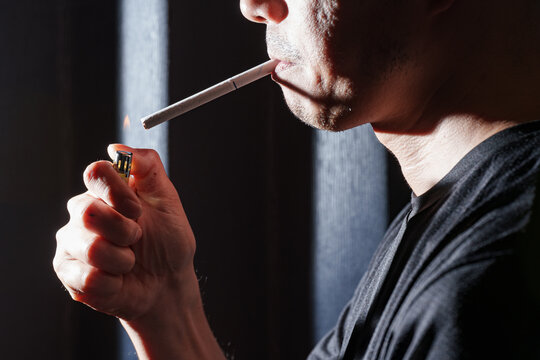ライターの火で紙タバコに点火する男性の口元。喫煙の始まりやストレスを象徴するシネマティック素材