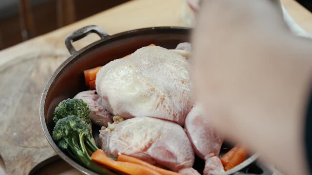 Close-up shot of raw chicken pieces and vegetables in a pot. Hands season the chicken with care. The scene feels warm and inviting, focused on home cooking. Great for recipes, food blogs