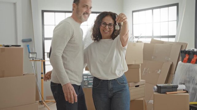 Man and woman embrace as she holds a house key aloft beside stacked moving boxes inside a building; new home joy.