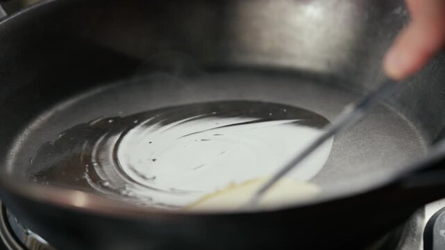 Butter melts in hot pan, knife gently slices through it. Smooth liquid spreads evenly across surface. Close-up highlights texture and sheen. Ideal for cooking tutorials, food blogs, or recipe videos