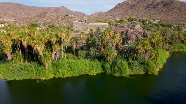 Aerial views show the mission of Santa Rosalia in Baja California Sur, Mexico, surrounded by mountains, desert, and palm trees in the late afternoon.