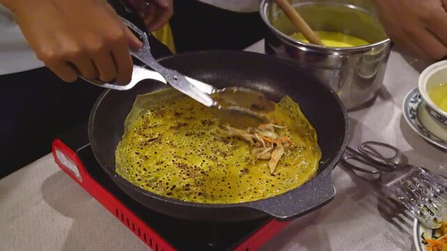 Traditional Vietnamese Banh Xeo crispy sizzling savory pancake being prepared in a pan, authentic Asian street food cooking process close-up.