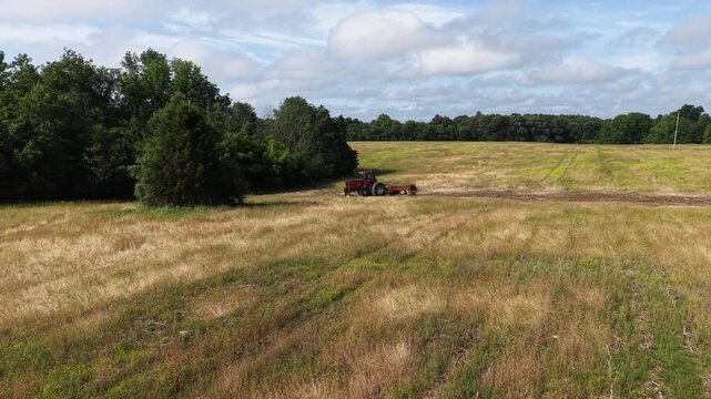 Agricultural tractor cultivating a field with a disc harrow on a cloudy summer day.