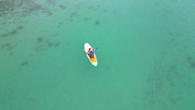 Top up aerial view of a father and his little daughter paddling together on a stand up paddleboard on the turquoise waters of Lake Kournas in Crete island, Greece. High quality 4k footage