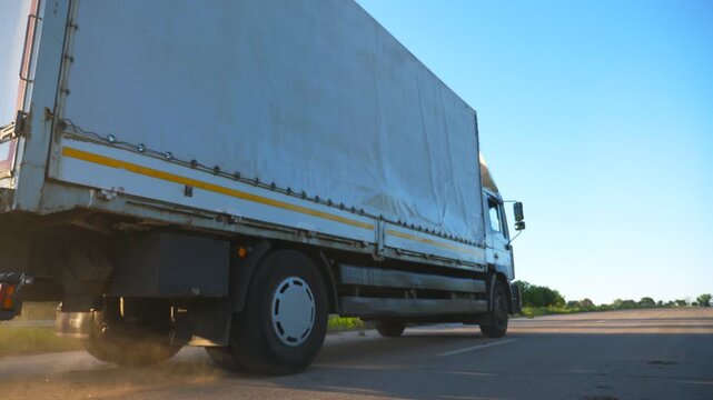 Close up of truck with cargo trailer driving on highway and transporting goods at evening time. White lorry speeding through country riding to destination. Slow motion Back Low view