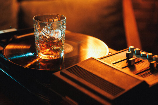 Whiskey drink on turntable beside mixer in warm neon lounge atmosphere. Concept of DJ night party, retro bar culture, premium beverage campaign, music event promo, and lounge advertising.