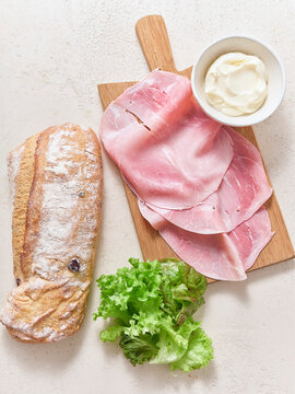 Preparation of a sandwich with ciabatta olive bread, sliced ham, lettuce, and mayonnaise during lunch time in a kitchen setting