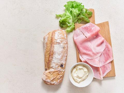 Making a sandwich with ciabatta olive bread, ham, lettuce, and mayonnaise on a flat surface viewed from above with space for text