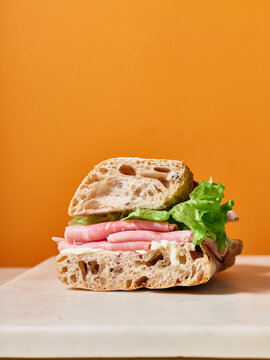 Ciabatta sandwich with ham and lettuce on a bright orange background for a simple meal or snack