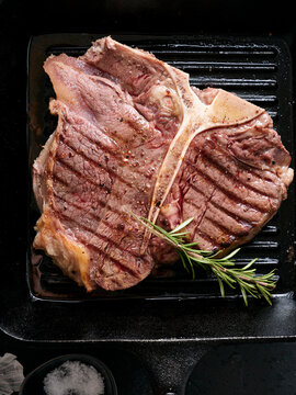 Grilled t-bone steak on a hot grill with marks and herbs at a kitchen setting during the afternoon meal preparation