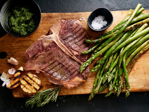 Grilled t-bone steak prepared with asparagus and seasoning on a wooden cutting board