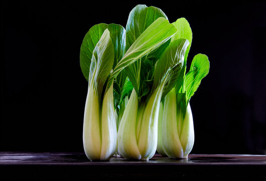 Fresh bok choy with vibrant green leaves on a dark wooden surface against black background.
