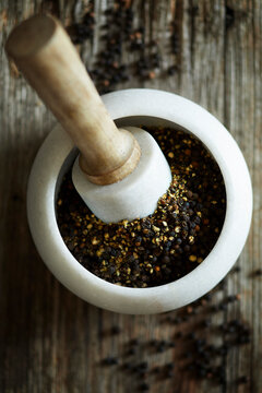 Freshly crushed black pepper in a stone mortar with wooden pestle on rustic wood.