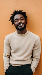 Fototapeta premium Smiling black man with dreadlocks leans against an orange wall, wearing a textured sweater and black pants, projecting confidence and style.