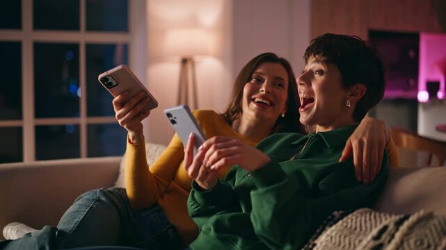 Laughing friends chilling with cellphones relaxing cozy home couch closeup. 