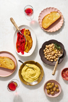 Angled shot of a bowl of braised butter beans with rosemary and lemon peel, some beans served onto toasted sourdough with saffron aioli and charred peppers, with plates of saffron aioli.