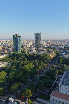 Tirane, Albania - 28 May 2026: Aerial view of a large crowd of people gathered in the city center near modern skyscrapers and lush green parks under a clear blue sky.